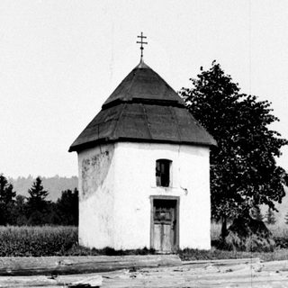 Small building with a spire near stacked logs and foliage.