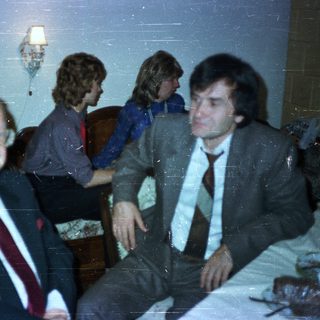 Men in suits and a woman seated in a room.