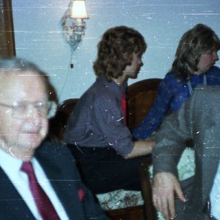 Men in suits and a woman seated in a room.