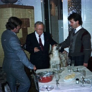 Three men and a dog at a formally set table.