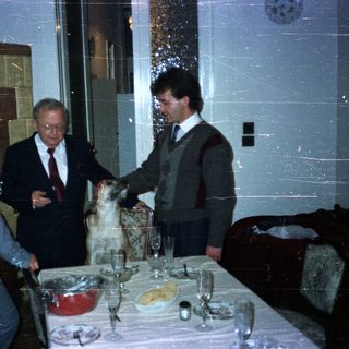 Three men and a dog at a formally set table.