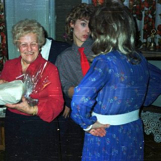 Woman receives gift, smiling, in a warmly decorated room.