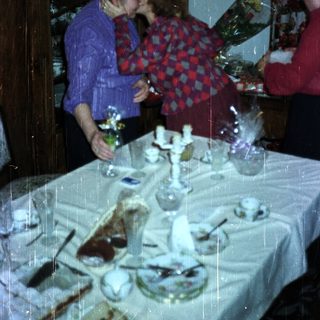 Two women embrace, gifts displayed on a decorated table.