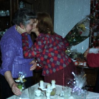 Two women embrace, gifts displayed on a decorated table.