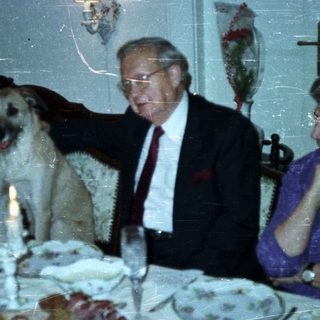 Couple and dog at a formally set dinner table.