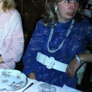 Women at a formal dinner table in a vintage setting.