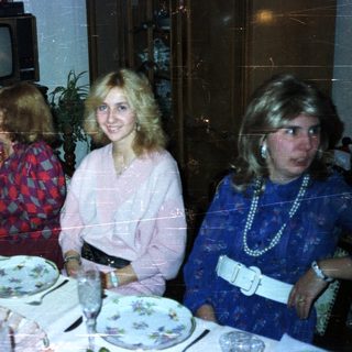 Women at a formal dinner table in a vintage setting.