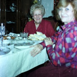 Two women seated at a table with a decorated sideboard.