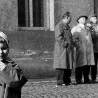 Here's a brief summary: Girl holds balloons, stands on cobblestone street.