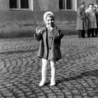 Here's a brief summary: Girl holds balloons, stands on cobblestone street.
