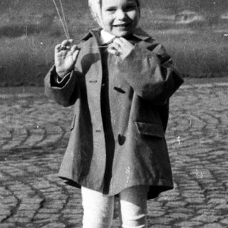 Here's a brief summary: Girl holds balloons, stands on cobblestone street.