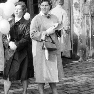 People holding balloons stand on a cobbled street.