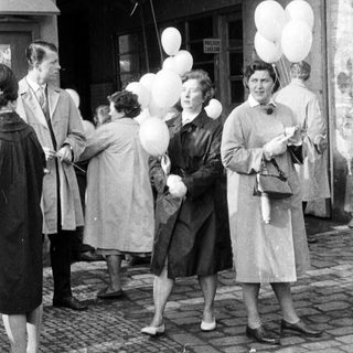 People holding balloons stand on a cobbled street.