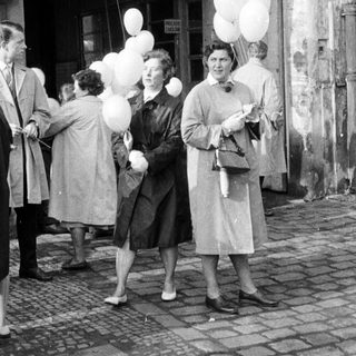 People holding balloons stand on a cobbled street.
