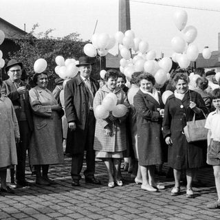 Group of people with balloons stands outdoors, possibly celebrating.