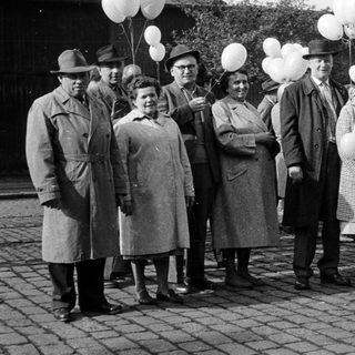 Group of people with balloons stands outdoors, possibly celebrating.