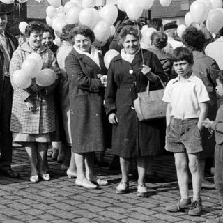 Group of people with balloons stands outdoors, possibly celebrating.