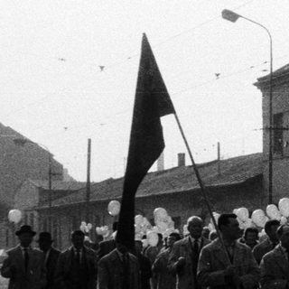 Parade with flags and banners on a cobblestone street.