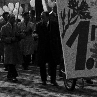 Parade with flags and banners on a cobblestone street.