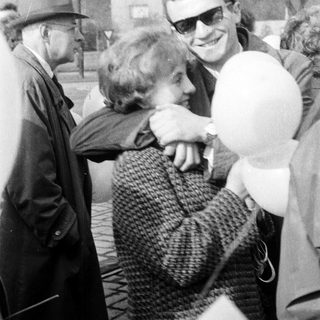 Man embraces a woman outdoors, holding a balloon.