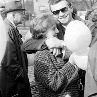 Man embraces a woman outdoors, holding a balloon.