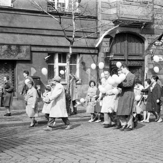 People on a street, many holding white balloons.