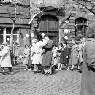 People on a street, many holding white balloons.