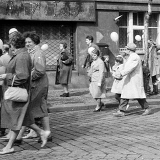 People on a street, many holding white balloons.