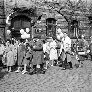 Group of people walk down a street with balloons.
