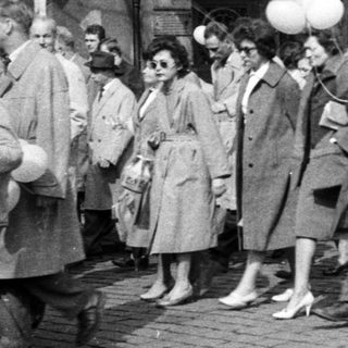 Group of people walk down a street with balloons.