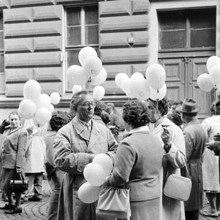 Group of people with balloons gathered outside a building.
