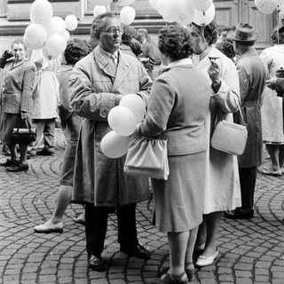 Group of people with balloons gathered outside a building.