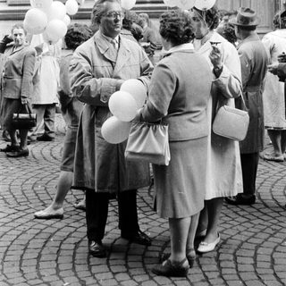 Group of people with balloons gathered outside a building.