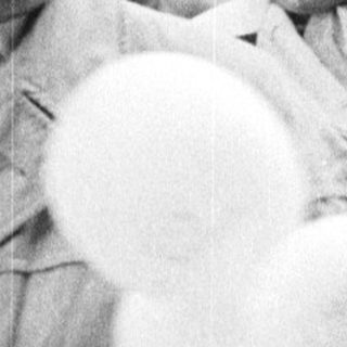 Man with balloons stands with women in a crowd.