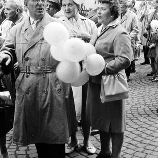 Man with balloons stands with women in a crowd.