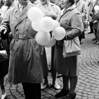 Man with balloons stands with women in a crowd.