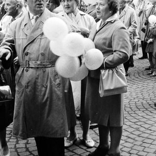 Man with balloons stands with women in a crowd.