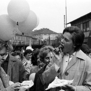 Black and white crowd with food, balloons, and buildings.