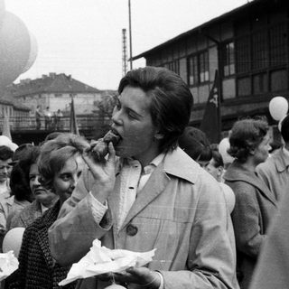 Black and white crowd with food, balloons, and buildings.