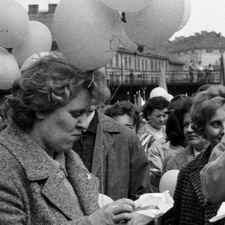 Black and white crowd with food, balloons, and buildings.