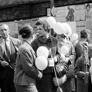 People holding balloons stand near a poster-covered wall.