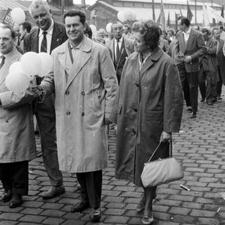 Couple walking on a cobblestone street with onlookers.