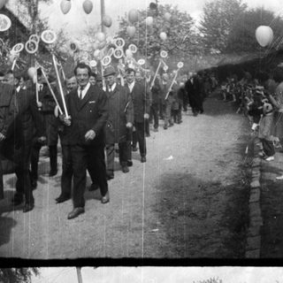 Parade or procession with people, flags, and balloons.