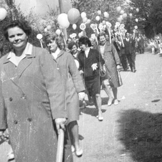 Parade or procession with people, flags, and balloons.