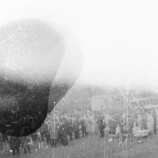 People watch airships or hot air balloons in a field.