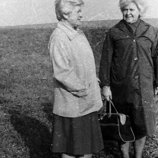 Two women in coats standing in a grassy field.