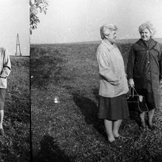 Two women in coats standing in a grassy field.