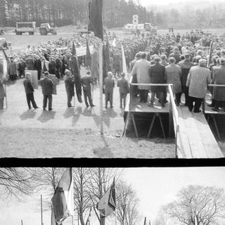 Parade or rally with flags and onlookers in a field.