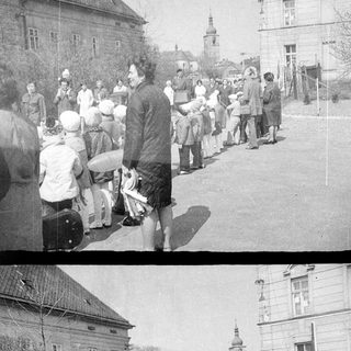 Here's a brief summary of the image: People gather on a street, possibly during a procession.