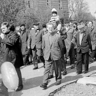 Here's a brief summary of the image: People gather on a street, possibly during a procession.